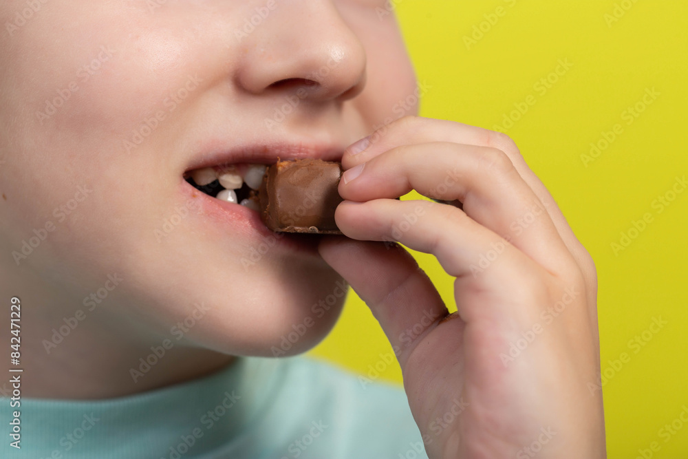 Beautiful little caucasian girl eating a chocolate bar on a yellow background. Sweet food, calories. Copy space for text Beautiful little caucasian girl eating a chocolate bar on a yellow background. Sweet food, calories. Copy space for text