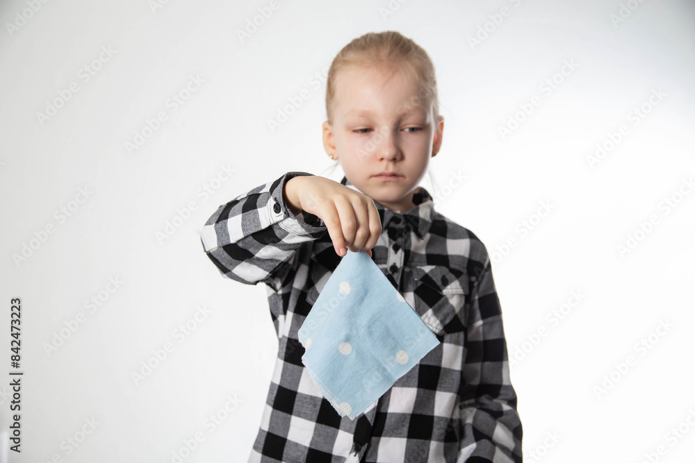 a sad girl aged seven years old holds a handkerchief in her hand against the background of a plaid shirt. Concept of runny nose and nasal congestion in children. Chronic rhinitis and sinusitis. a sad girl aged seven years old holds a handkerchief in her hand against the background of a plaid shirt. Concept of runny nose and nasal congestion in children. Chronic rhinitis and sinusitis.