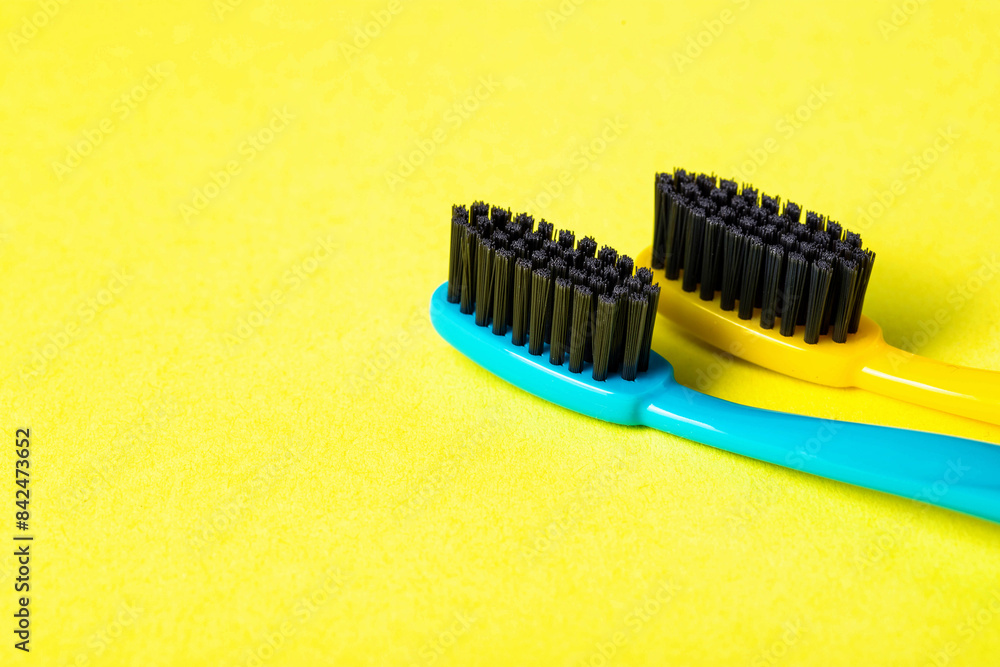 Two toothbrushes with black charcoal hard bristles on a yellow background, close-up. The concept of hygiene and teeth cleaning in dentistry, macro. Copy space for text Two toothbrushes with black charcoal hard bristles on a yellow background, close-up. The concept of hygiene and teeth cleaning in dentistry, macro. Copy space for text