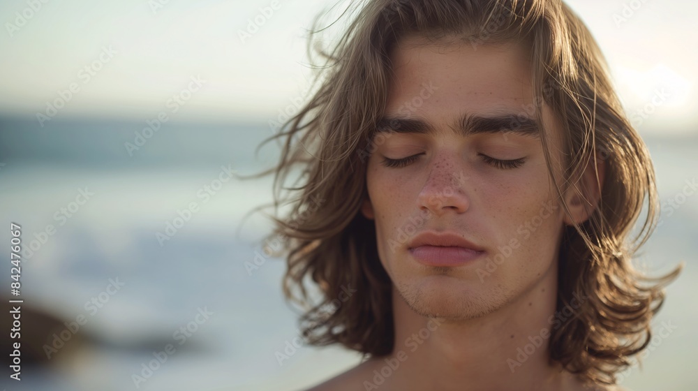 close-up portrait of a young man with long, wavy hair standing on a beach.