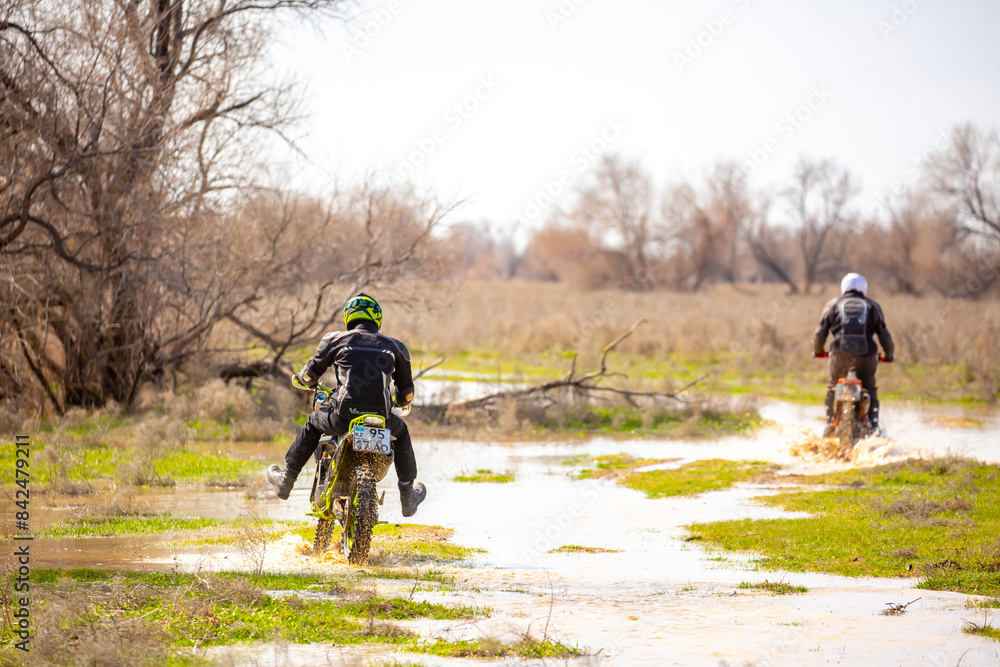 Fototapeta premium A motorcyclist rides an enduro motorcycle off-road. Driving through swampy areas, water and mud splashing from under the wheels. Kazakhstan, Shymkent - April 17, 2024