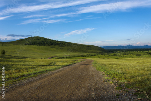 A dirt road leading to green hills against a blue sky