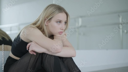 Fit girl in black clothes performing contemporary. Female dancer shows flowing motions, body and hands waves at white room. Modern ballet dance choreography. Young woman is moving smoothly photo