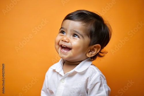 A precious Indian toddler in a white shirt giggles infectiously against a soft orange backdrop, indian, toddler, baby, child, laugh, smile, happy, cute, adorable, sweet, joy, innocence photo