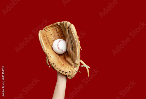 Photography Hand in leather baseball glove holds white baseball on red background