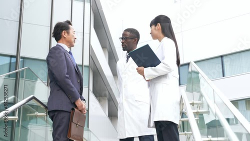 ロビーで会話するビジネスマンと白衣の多国籍技術者グループ photo