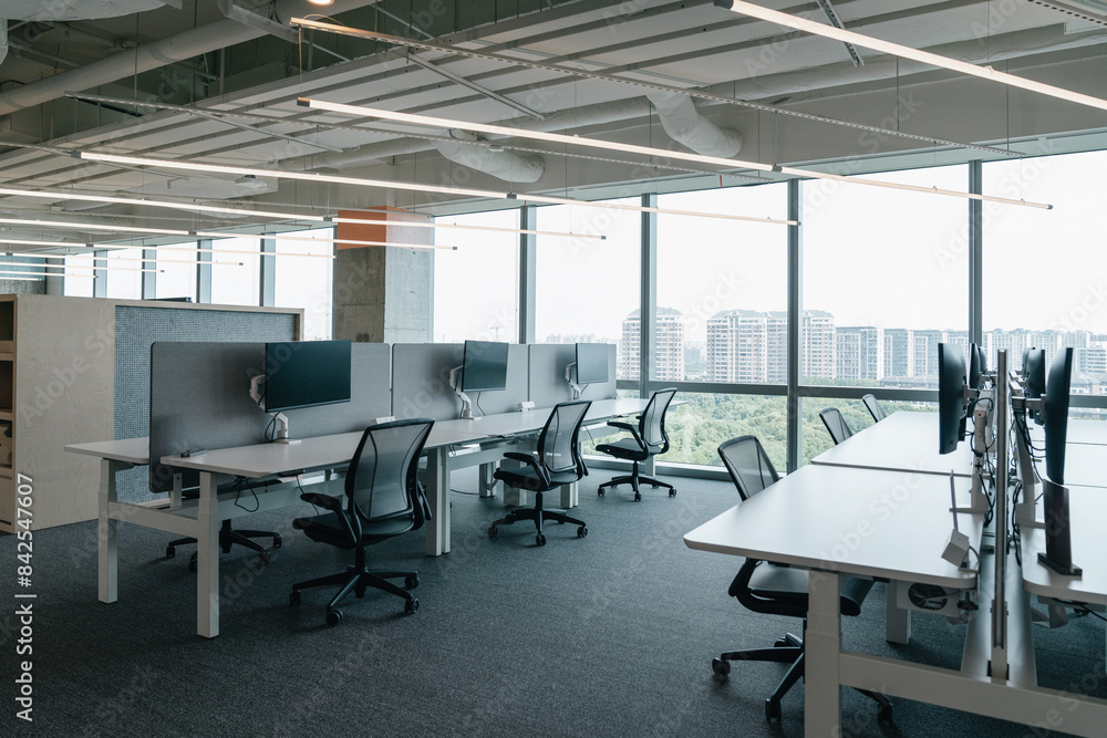 A modern, open-plan office space filled with natural light from large windows that offer a view of the cityscape. The office features a clean, minimalistic design with chairs and computer monitors. A modern, open-plan office space filled with natural light from large windows that offer a view of the cityscape. The office features a clean, minimalistic design with chairs and computer monitors.