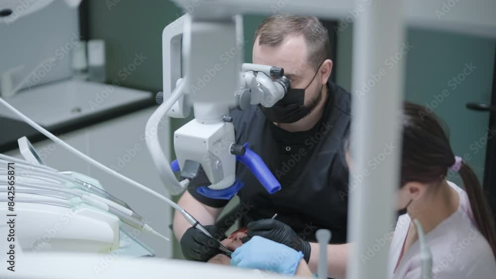 Male dentist working with dental microscope in modern stomatology clinic. Doctor using microscope for root canal treatment. Stomatologist performs a surgical operation. Cosmetic dentistry and surgery. Male dentist working with dental microscope in modern stomatology clinic. Doctor using microscope for root canal treatment. Stomatologist performs a surgical operation. Cosmetic dentistry and surgery.
