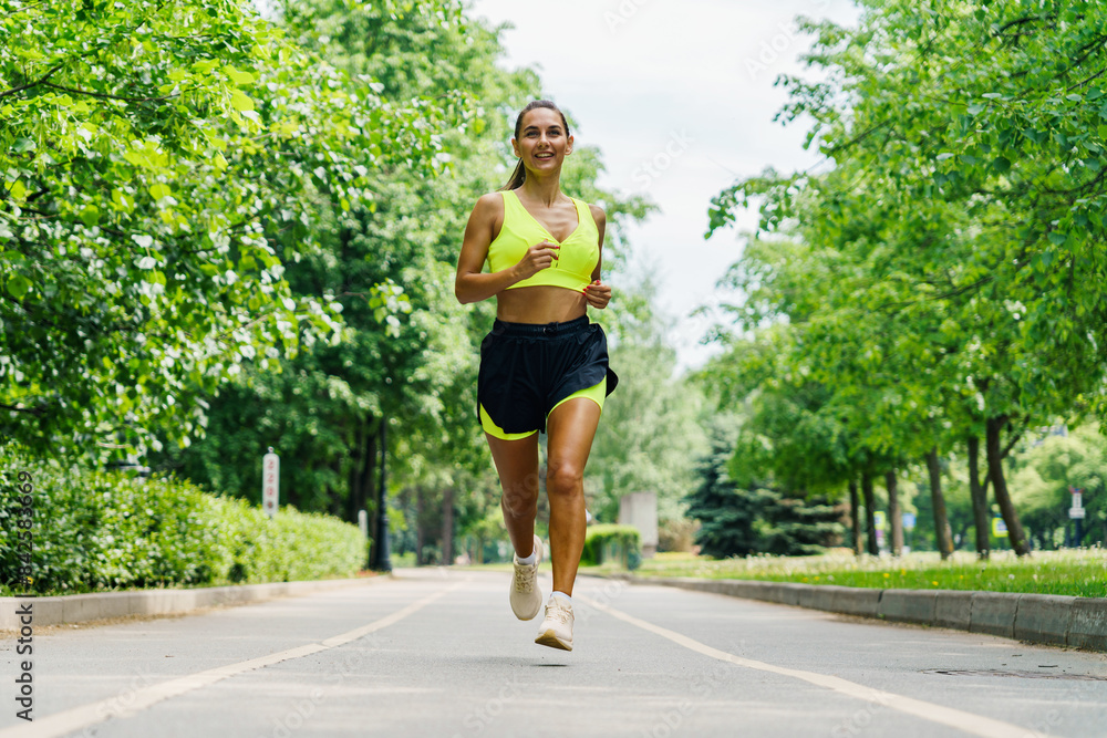 A young woman jogs along a sunlit path lined with lush green trees, embodying health and vitality. A young woman jogs along a sunlit path lined with lush green trees, embodying health and vitality.
