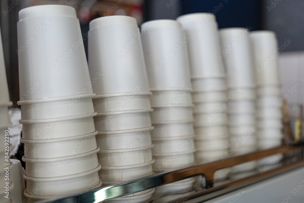 A lot of white disposable paper cups on coffee machine. The stack of paper cup in the cafe A lot of white disposable paper cups on coffee machine. The stack of paper cup in the cafe