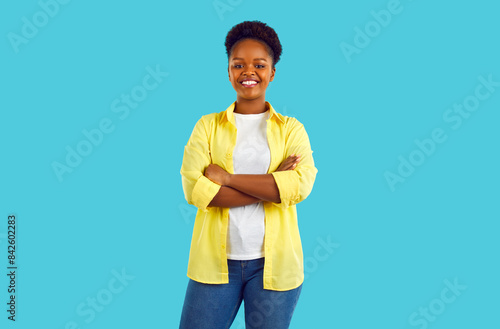 Attractive african woman with short hair in a white T-shirt, yellow shirt and blue jeans.Smiling at the camera with his arms crossed, posing on a blue background.The snow-white smile of the model.