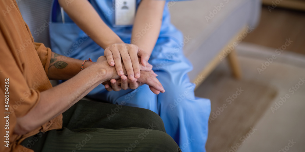 Fototapeta premium Close up of Asian caregiver holding hands with elderly woman at home. Concept of compassion and support