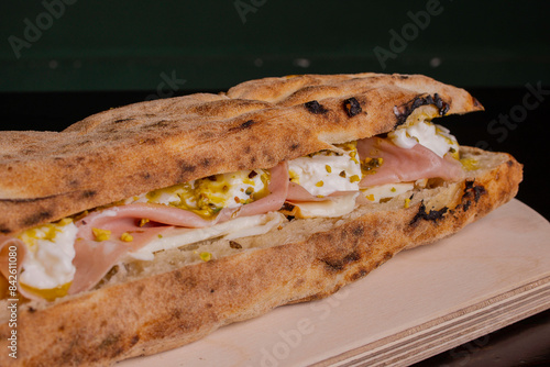 Panuozzo tradizionale campano ripieno di mortadella, ricotta, mozzarella e granella di pistacchio servito in un pub su un tagliere di legno photo