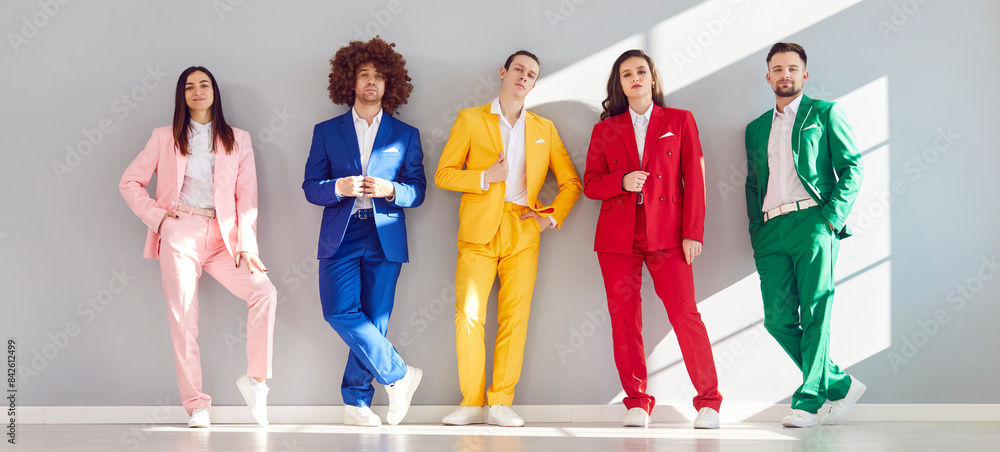 Portrait of a group of young business team in colorful suits standing against a grey wall. The image captures smiling faces, reflecting diverse and happy teamwork in a business setting. Portrait of a group of young business team in colorful suits standing against a grey wall. The image captures smiling faces, reflecting diverse and happy teamwork in a business setting.