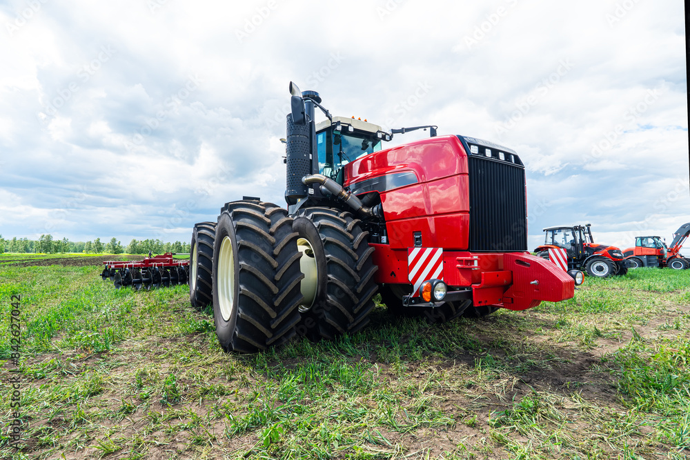 Obraz premium Close up of agriculture red tractor cultivating field over blue sky