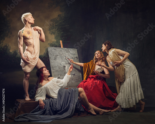 Muscular man with posing wrapped transparent fabric, while three women painting his portrait against vintage background. Neo-Classical scene. Concept of comparisons of eras, classical art, renaissance photo