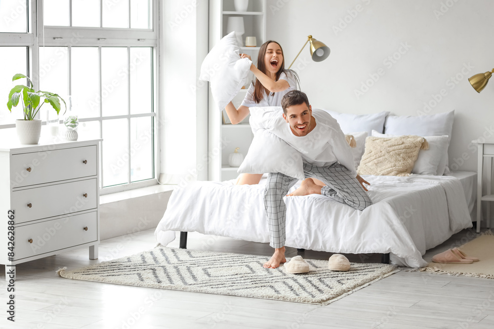 Young woman with her husband fighting pillows in bedroom Young woman with her husband fighting pillows in bedroom