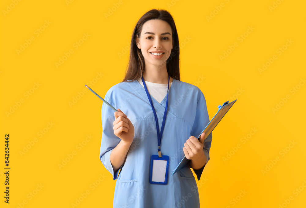 Young female doctor with clipboard and pen on yellow background Young female doctor with clipboard and pen on yellow background