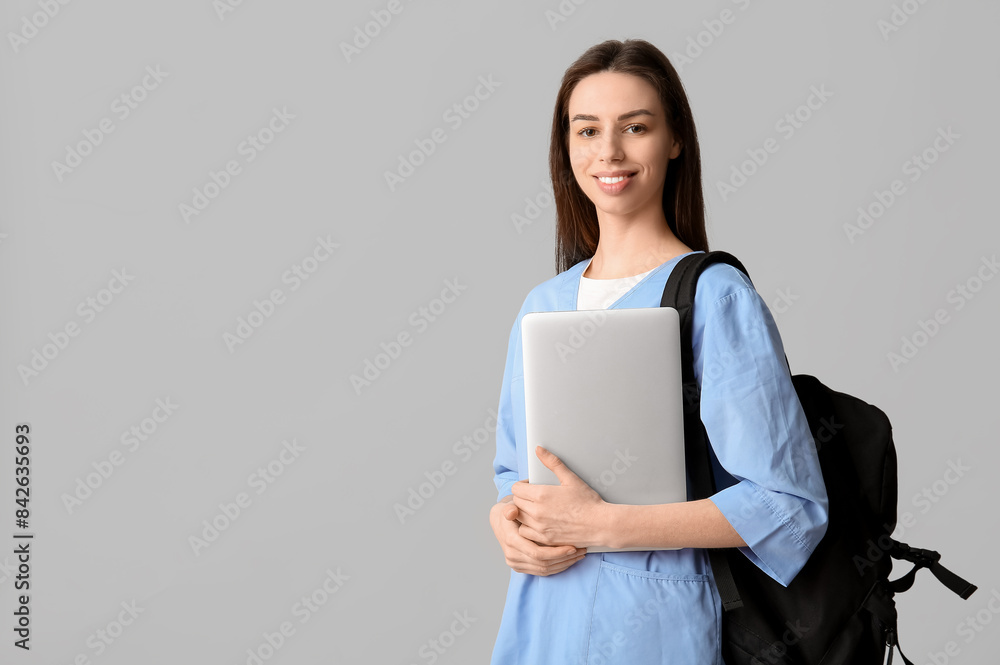 Young female doctor with laptop and backpack on grey background Young female doctor with laptop and backpack on grey background