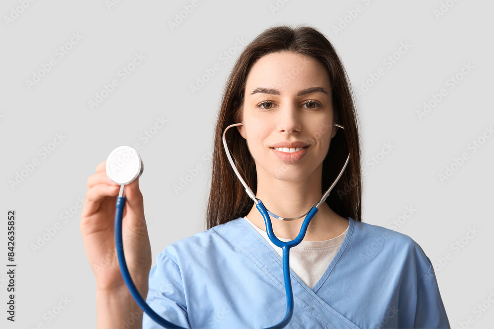 Young pretty female doctor with stethoscope on grey background Young pretty female doctor with stethoscope on grey background