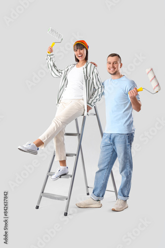 Young couple with paint rollers and stepladder on light background. Repair concept