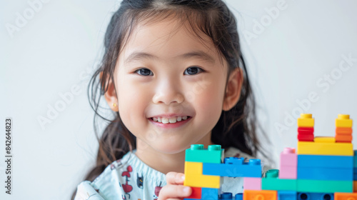 A smiling little girl holding Lego blocks with a white backdrop.