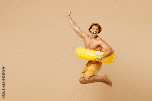 Full body young man wears yellow shorts swimsuit hat relax rest near hotel pool jump in inflatable ring do winner gesture isolated on plain beige background. Summer hot vacation sea sun tan concept.