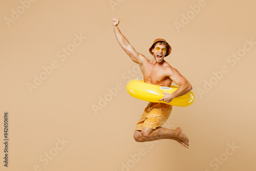 Foto Full body young man wears yellow shorts swimsuit hat relax rest near hotel pool jump in inflatable ring do winner gesture isolated on plain beige background