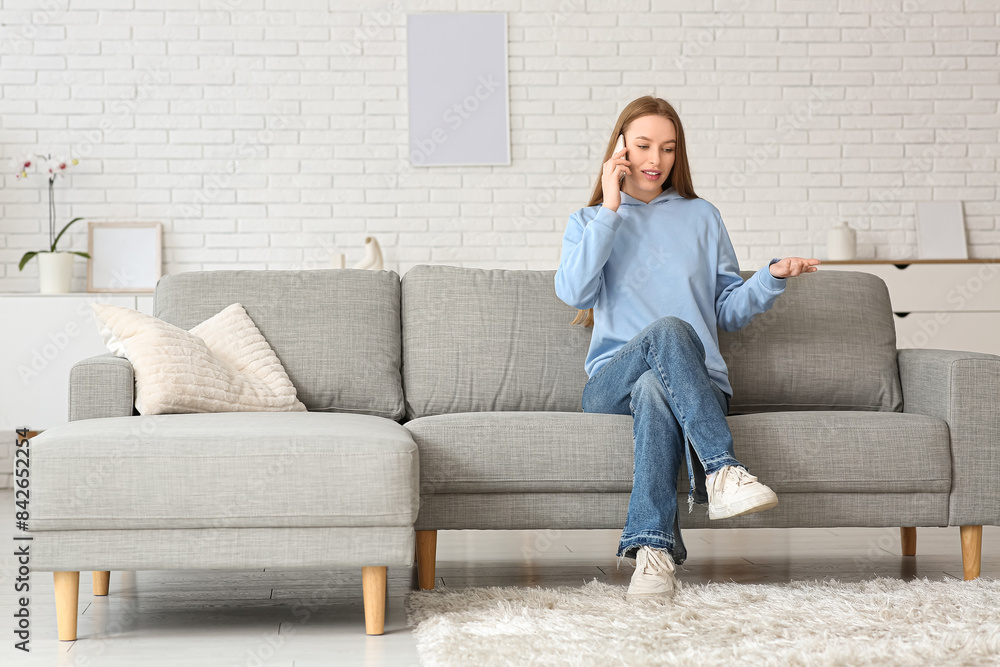 Obraz premium Young pretty woman talking with mobile phone on sofa in stylish living room