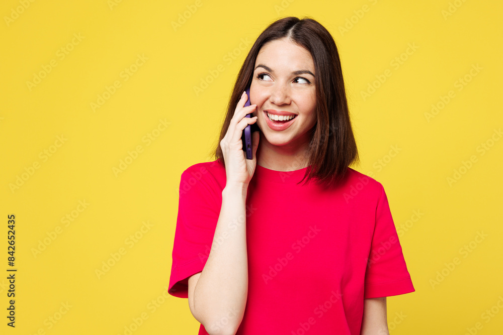 Young happy woman she wear pink t-shirt casual clothes talk speak on mobile cell phone conducting pleasant conversation isolated on plain yellow orange background studio portrait. Lifestyle concept. Young happy woman she wear pink t-shirt casual clothes talk speak on mobile cell phone conducting pleasant conversation isolated on plain yellow orange background studio portrait. Lifestyle concept.