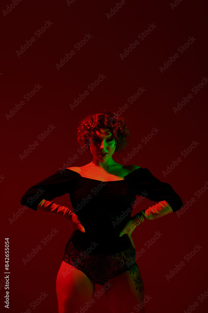 A young curvy redhead woman wearing a black dress, standing confidently in front of a striking red background. A young curvy redhead woman wearing a black dress, standing confidently in front of a striking red background.