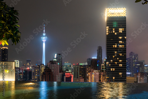 Photography Kuala Lumpur's night skyline with the illuminated KL Tower and Pavilion Tower reflecting on water, showcasing the city's iconic architecture and vibrant atmosphere