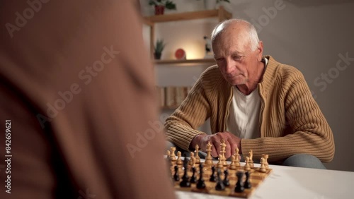 A senior man is fully engaged in a game of chess, deep in thought, in the comfort of his home photo