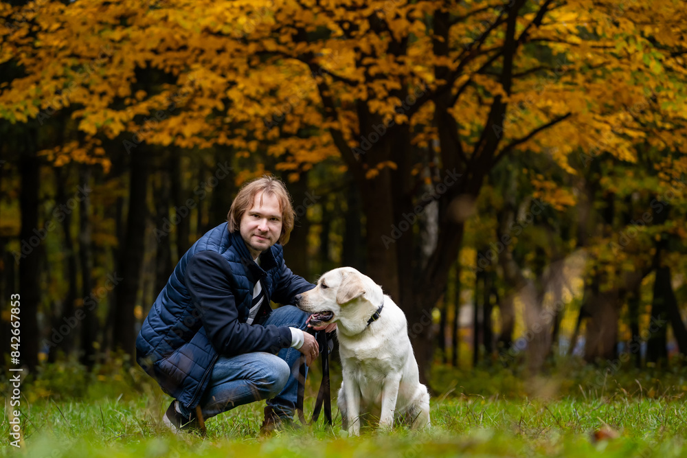 A man and his dog are standing in a grassy field with trees in the background. The man is wearing a blue jacket and jeans A man and his dog are standing in a grassy field with trees in the background. The man is wearing a blue jacket and jeans