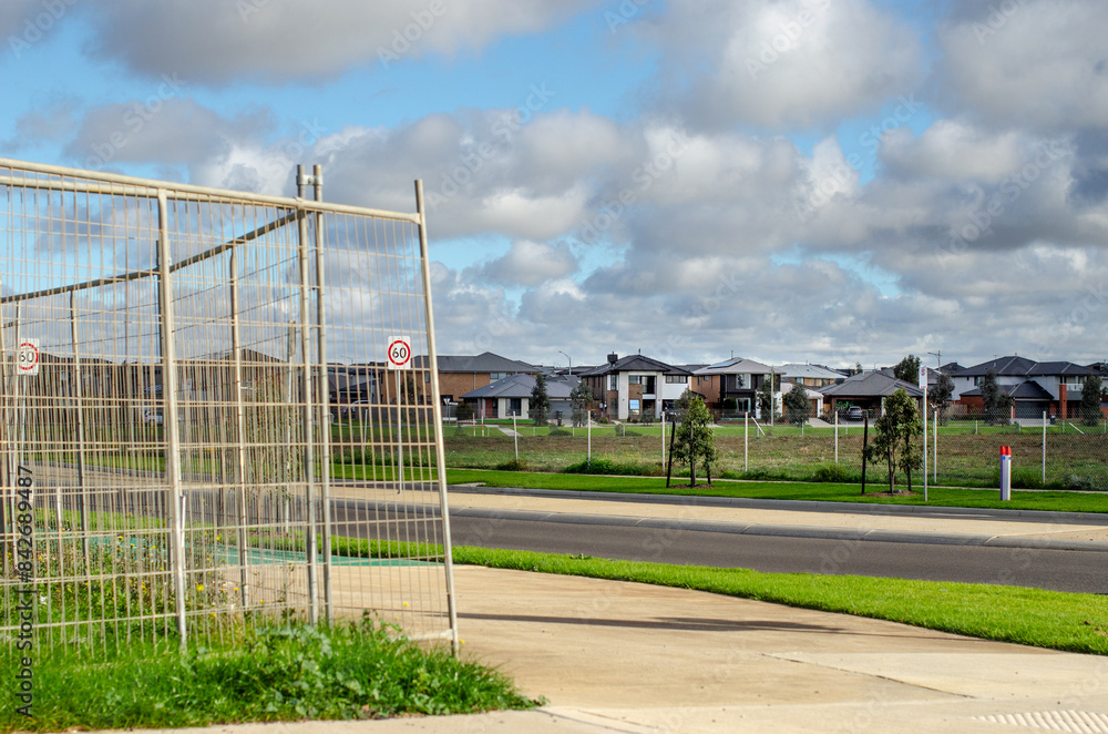 A newly developed suburb with rows of modern Australian residential houses in the distance at Melbourne’s outskirts, with a construction site fence in the foreground. Werribee, VIC, Australia. A newly developed suburb with rows of modern Australian residential houses in the distance at Melbourne’s outskirts, with a construction site fence in the foreground. Werribee, VIC, Australia.