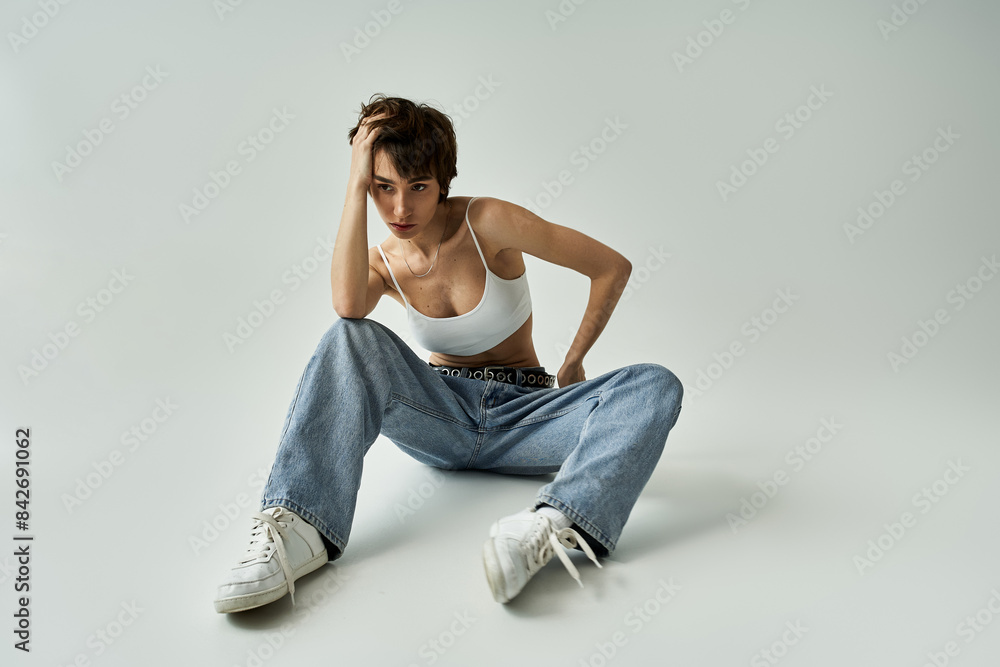 Young woman in jeans and white tank top sits on the floor in a stylish pose. Young woman in jeans and white tank top sits on the floor in a stylish pose.
