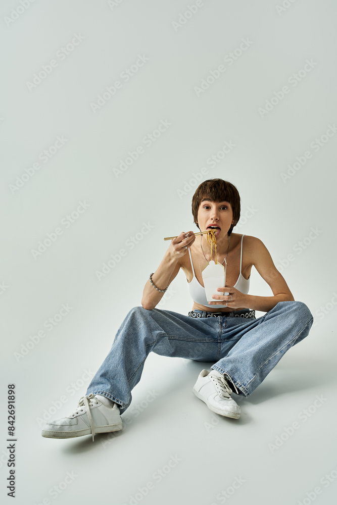 A stylish young woman sitting on the floor enjoying a tasty noodles. A stylish young woman sitting on the floor enjoying a tasty noodles.