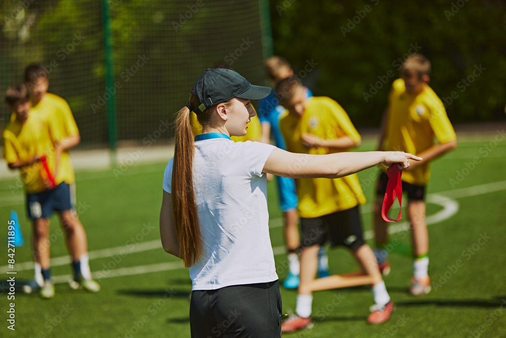 Fototapeta premium Group of young athletes, children training football outdoors with female coach on warm sunny day. Hobby and teamwork. Concept of sport, school, childhood, achievements, active lifestyle