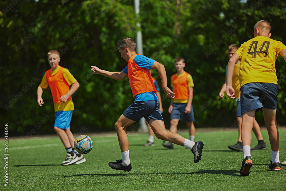 Obraz premium Teamwork in Action. Young soccer players in colorful uniforms playing soccer game outdoors on sunny day. Cooperation and competitive spirit. Sport, school, childhood, hobby, active lifestyle concept