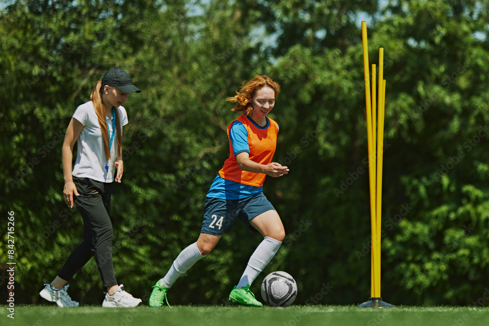 Obraz premium Skill Development on the Field. Female soccer player in bright sportswear training with her coach providing guidance to enhance her performance. Concept of sport, school, childhood, active lifestyle