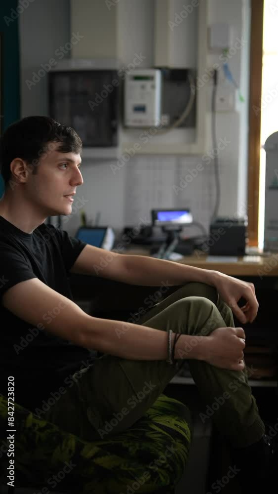 Young man in office, deep in thought, surrounded by technology, showing a contemplative attitude Young man in office, deep in thought, surrounded by technology, showing a contemplative attitude