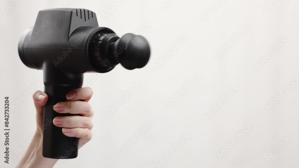 Close-up of woman's hand holding percussion massager with ball nozzle and turning it on gray background. Therapy for joint pain relief and physiotherapy Close-up of woman's hand holding percussion massager with ball nozzle and turning it on gray background. Therapy for joint pain relief and physiotherapy