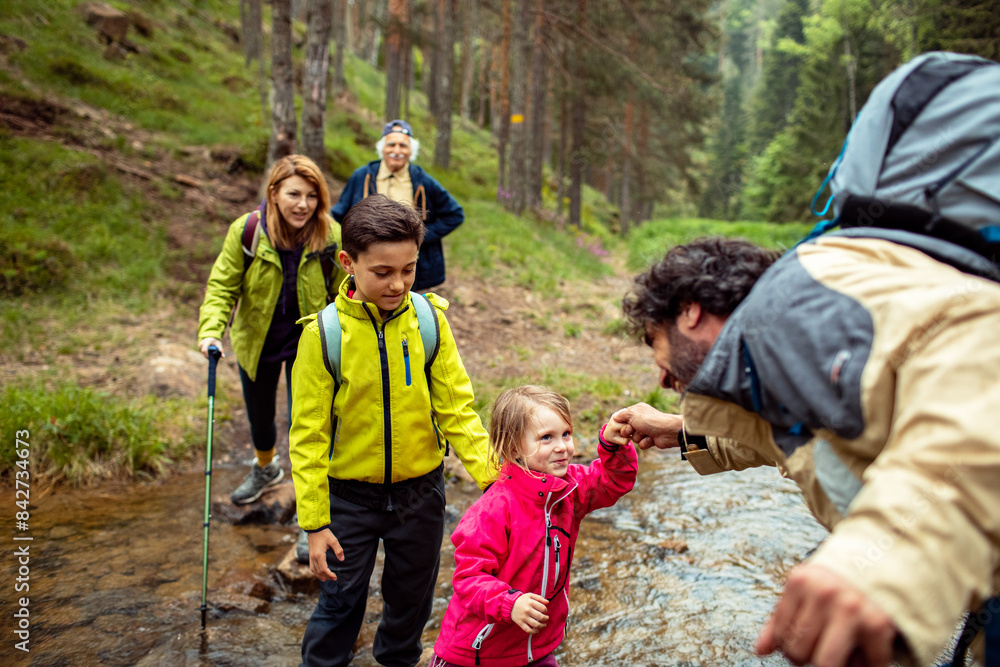 Multi-generational family crossing a stream during a forest hike Multi-generational family crossing a stream during a forest hike