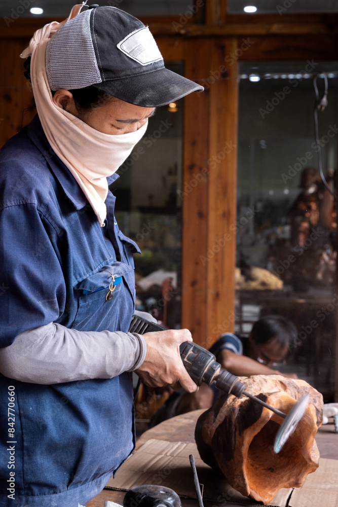 Fototapeta premium Vertical photo of a woman with her face covered working in a wood workshop.
