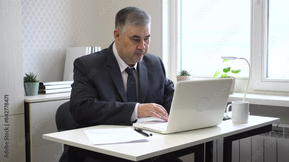 A man in a suit and tie works in the office. He types on the computer and makes notes on papers. The video is suitable for content about working in the office, running a business or remote work. A man in a suit and tie works in the office. He types on the computer and makes notes on papers. The video is suitable for content about working in the office, running a business or remote work.