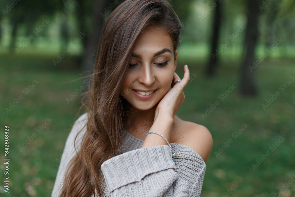 Happy beautiful young fresh girl with a cute smile model in a fashion knitted sweater walks in the park in nature Happy beautiful young fresh girl with a cute smile model in a fashion knitted sweater walks in the park in nature