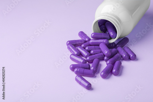 Purple pill capsules spilling out of drug bottle on purple background