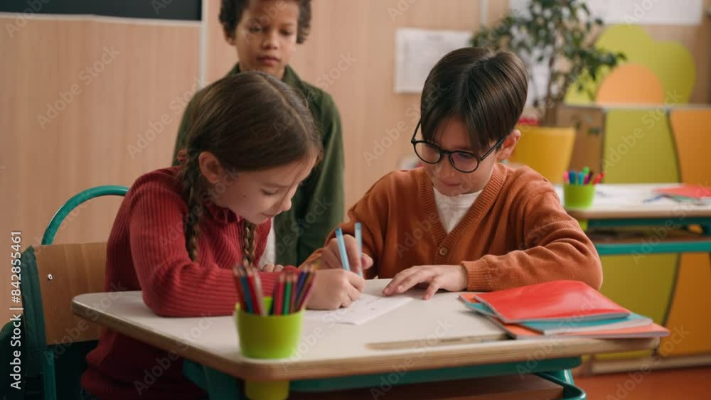 Two Caucasian children school lesson girl boy classmates drawing writing in notebooks African American kid child schoolboy approach look at picture dissatisfied mock talking pointing bullying go away Two Caucasian children school lesson girl boy classmates drawing writing in notebooks African American kid child schoolboy approach look at picture dissatisfied mock talking pointing bullying go away