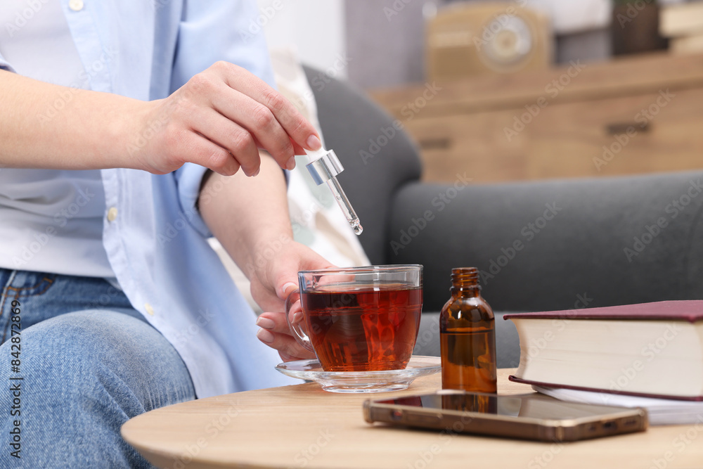 Woman dripping food supplement into cup of tea at wooden table indoors, closeup Woman dripping food supplement into cup of tea at wooden table indoors, closeup
