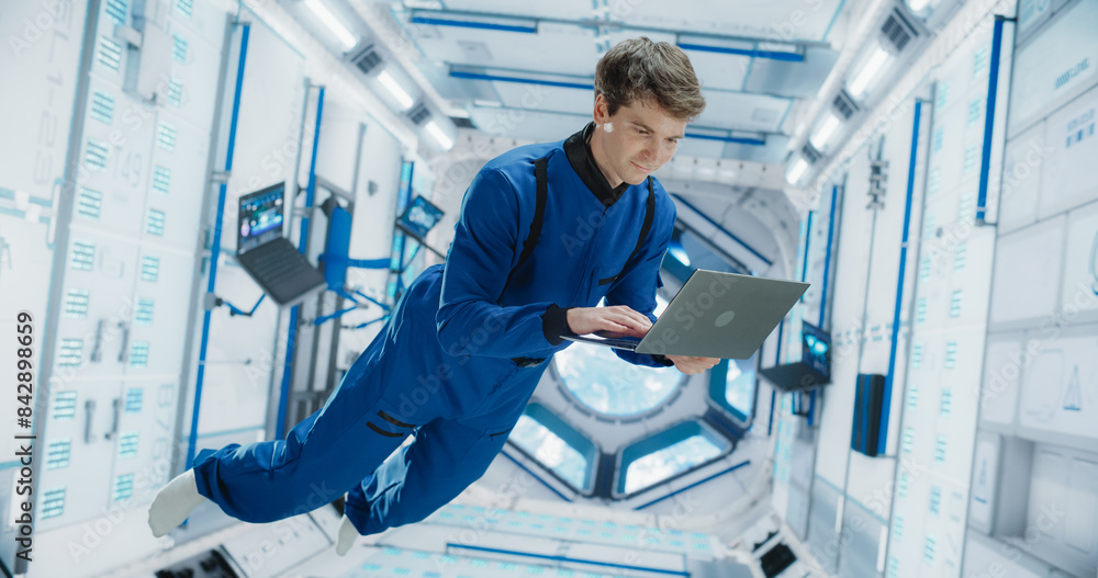 Caucasian Male Astronaut Using Laptop to Wirelessly Connect to a Satellite. Scientist Working on Computer Device Inside an Intergalactic Station. Professional Engineer Undertaking Service Job Caucasian Male Astronaut Using Laptop to Wirelessly Connect to a Satellite. Scientist Working on Computer Device Inside an Intergalactic Station. Professional Engineer Undertaking Service Job